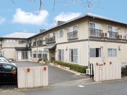 駐車場が付いた2階建てのホーム。建物の周りには木が植えられ、鉢が置かれている。