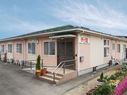 平屋建ての建物は薄いオレンジとベージュでまとめられ、花壇にはたくさんの花が咲いている。