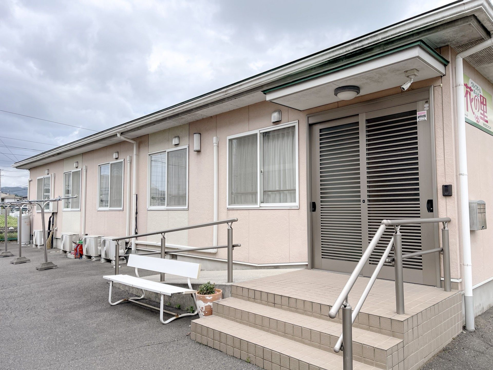 平屋建ての建物には瓦屋根が付き、玄関先には階段とスロープが付いている。