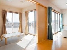 畳敷きの和室とフローリングのリビングダイニングがつながっている。和室には長方形のローテーブルが置かれ、窓には色の異なるカーテンが付いている。
