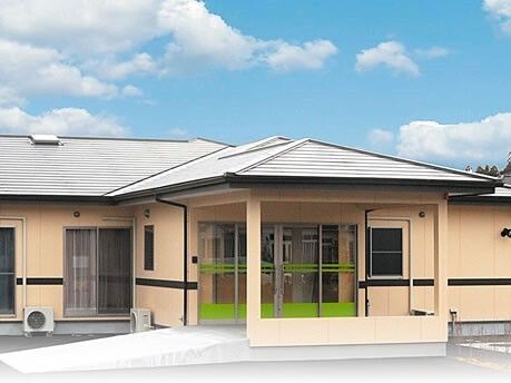 平屋建ての建物はベージュの外壁でグレーの三角の屋根が付き、玄関にはライトグリーンのラインが入ったガラスの自動ドアが設置されている。
