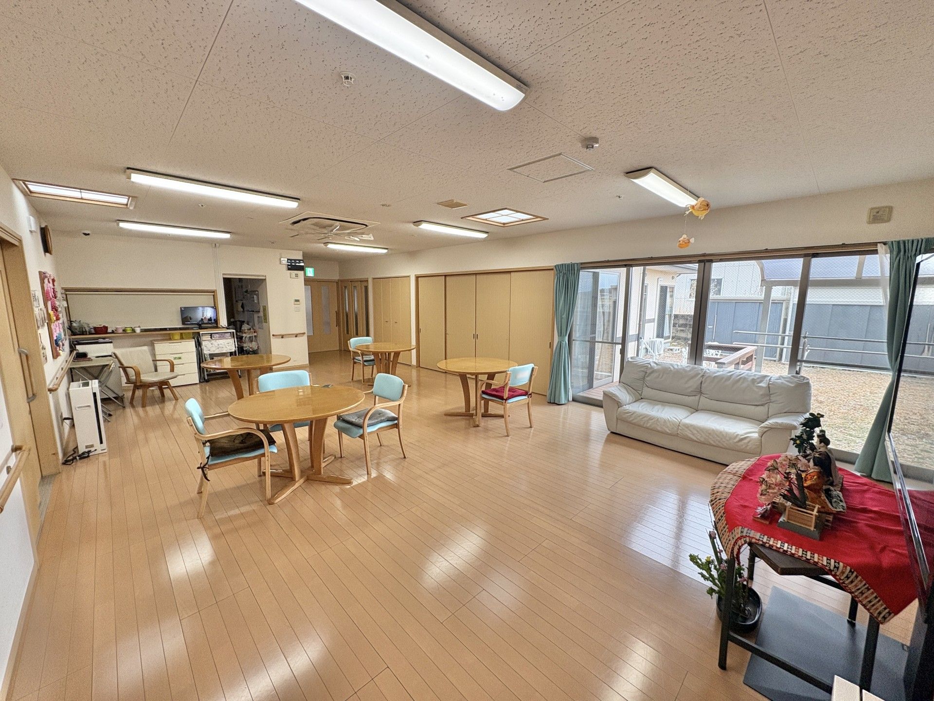 4人掛けのダイニングテーブルがたくさん置かれたリビングダイニング。大きな窓のそばには外を見ることができるよう、白いソファも置かれている。