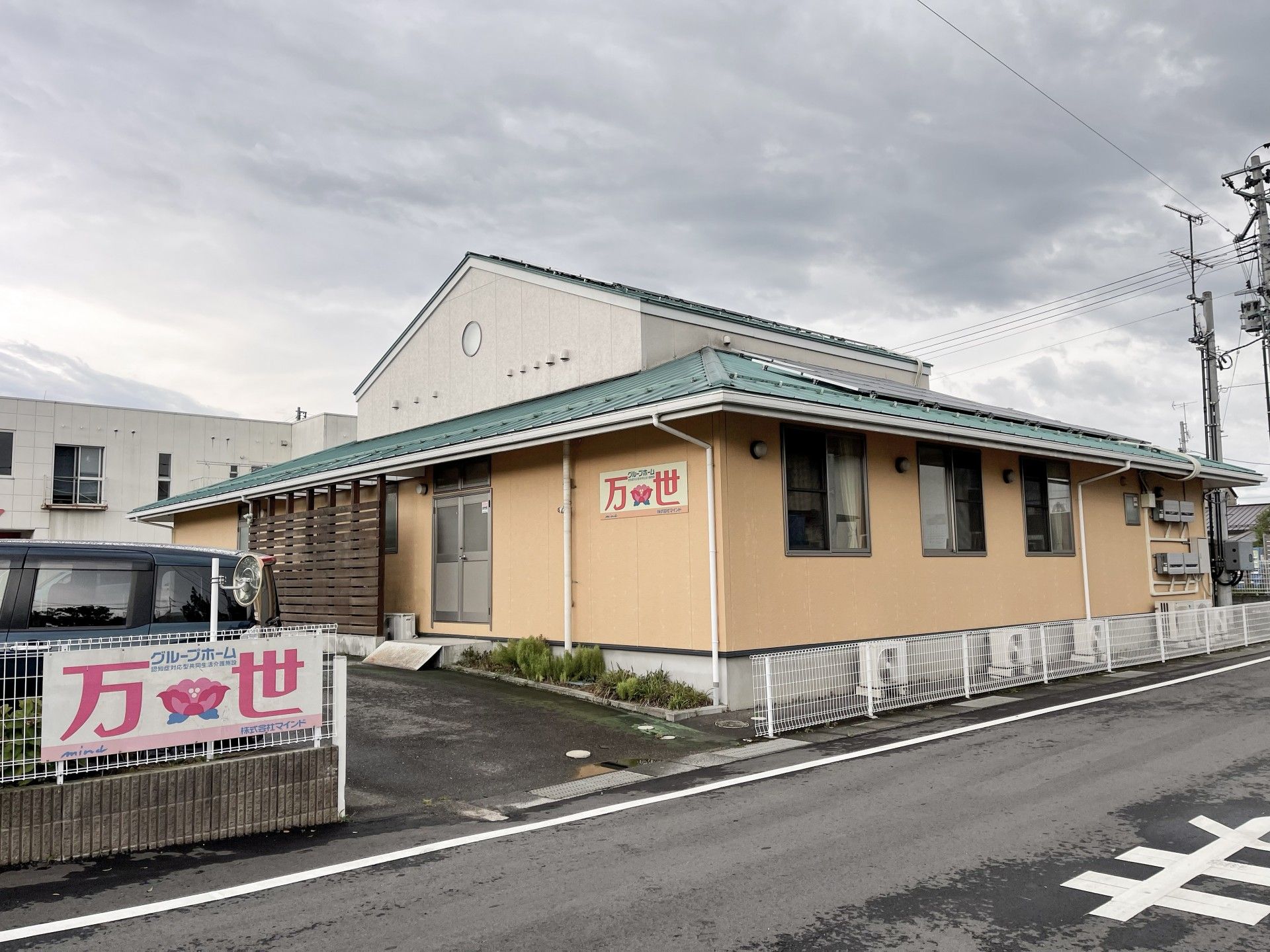 緑の屋根の建物はアットホームな雰囲気。花壇には花が植えられ、駐車スペースもある。