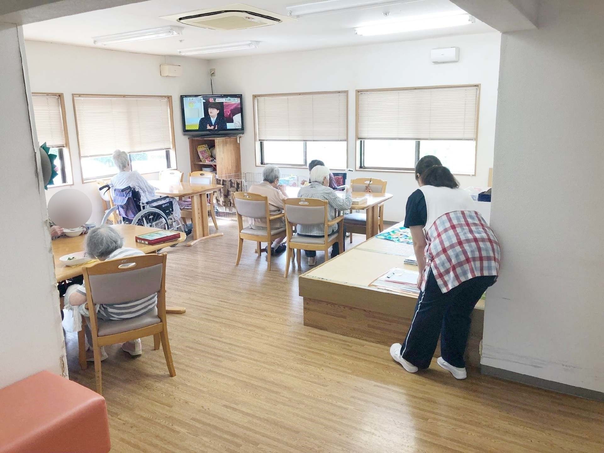 テレビが置いてある広めのホールに高齢者が集まりくつろいでいる様子。たたみのこあがりがあるリラックススペース