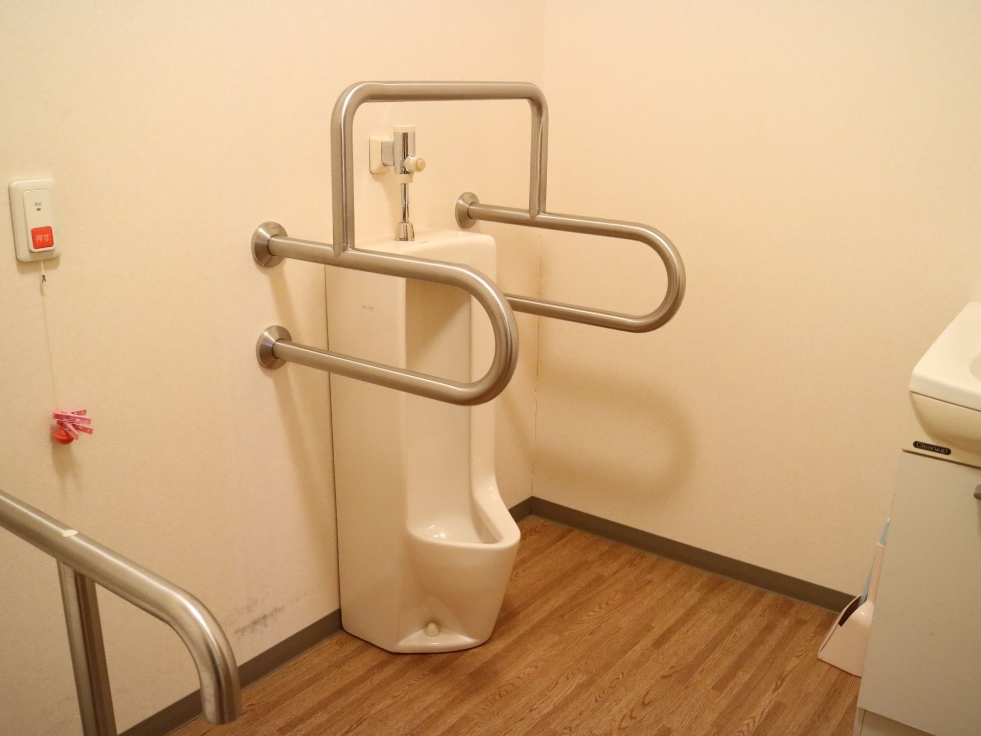 男性用トイレには便器の周りに銀色の手すりがある。緊急時に備えて、壁には呼び出しボタンがついている。