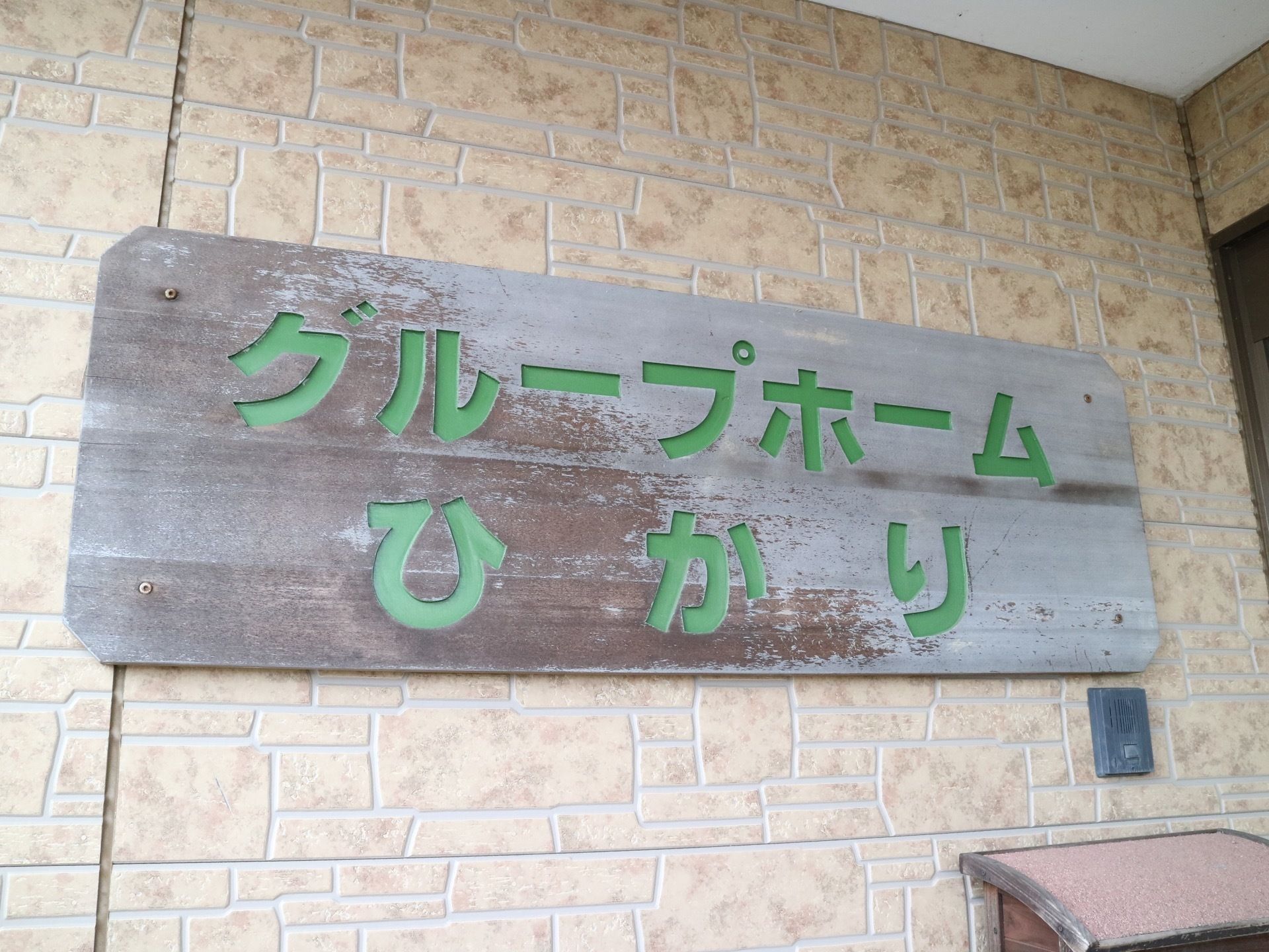 施設の入口に施設名のプレートが掲げられている。灰色の横長の板に緑色の文字で施設の名称が書かれている。