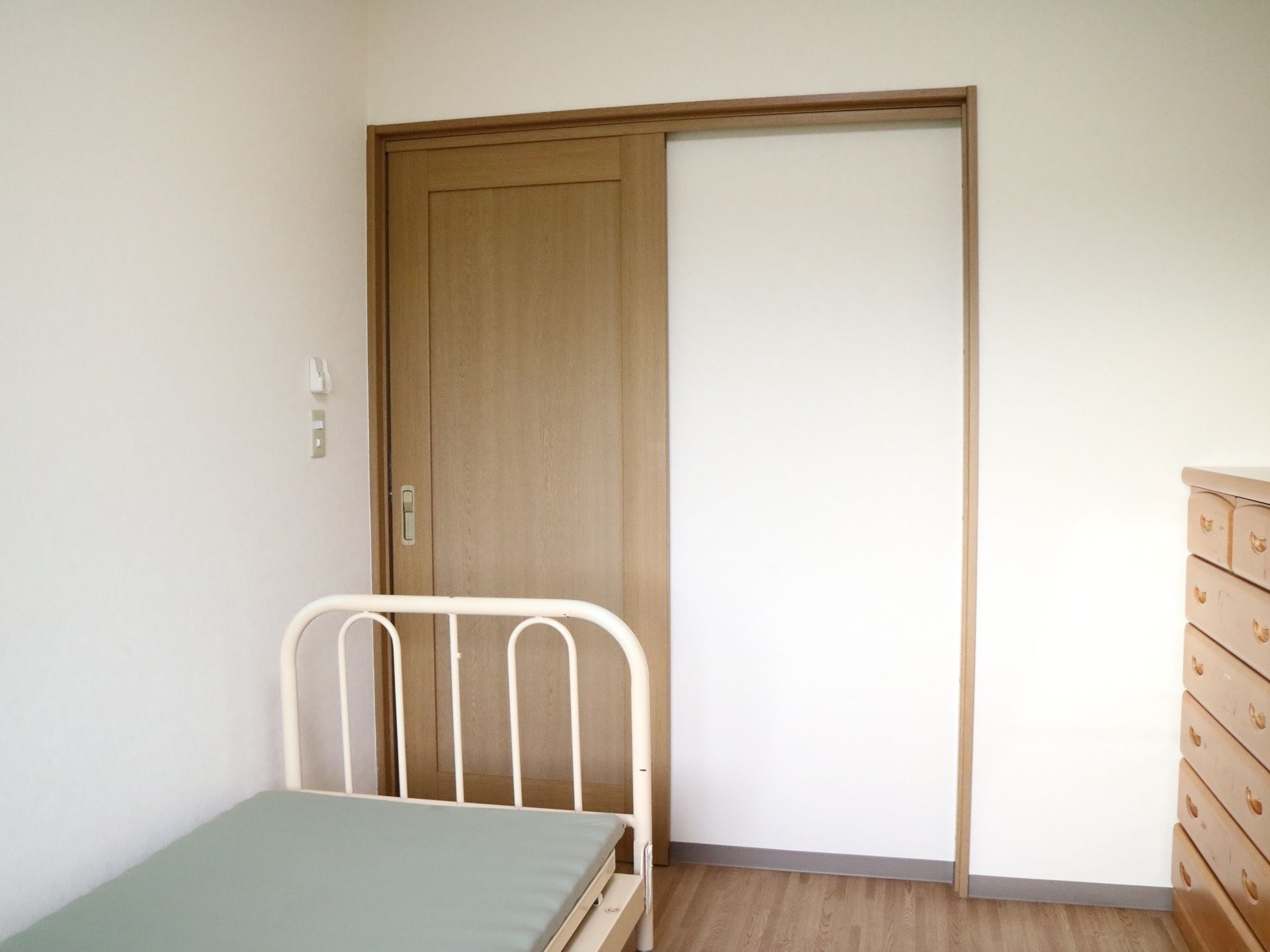 居室のドアはスライドタイプで、開け閉めしやすい。茶色いタンスがあり、引き出しが数多くついている。ベッドも設置されている。