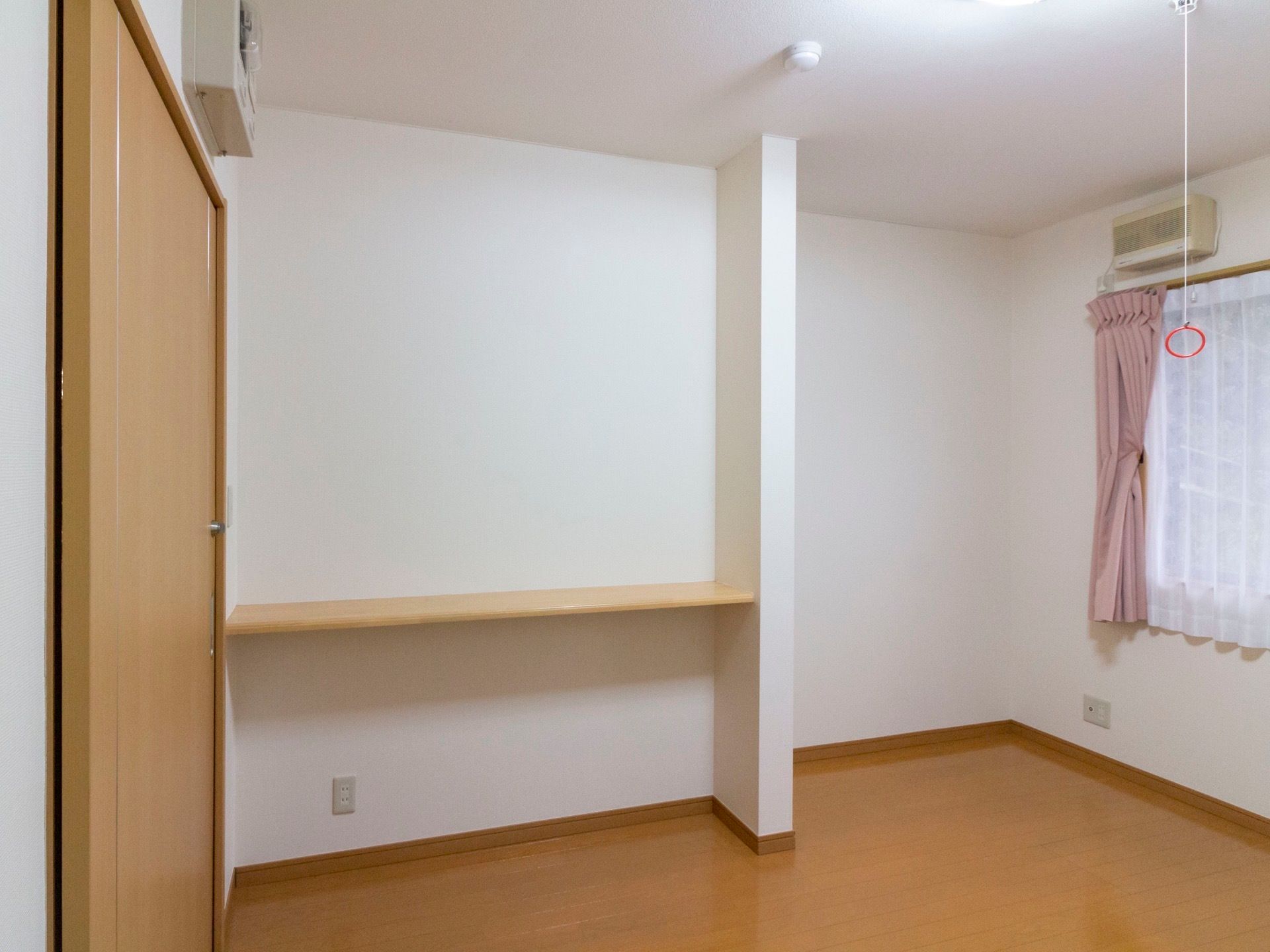 白色と木目調のデザインの居室である。ドア横の壁際には木の板で仕切られた収納スペースがあり、物が置けるようになっている。