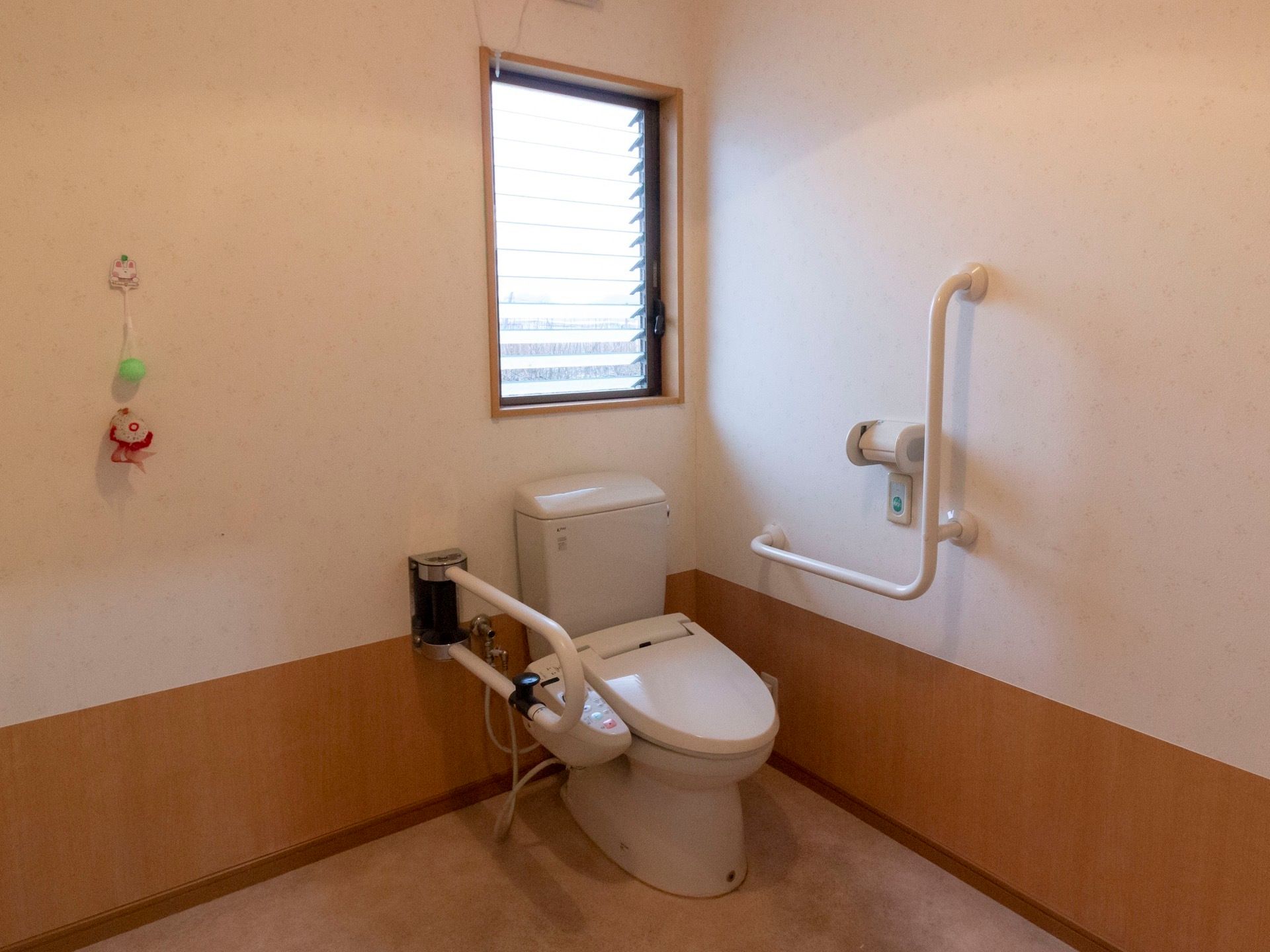 当施設のトイレの様子である。温水洗浄便座仕様でいつも清潔に使用することができる。便座の両脇に手すりがあり、立ち座りの際に便利である。