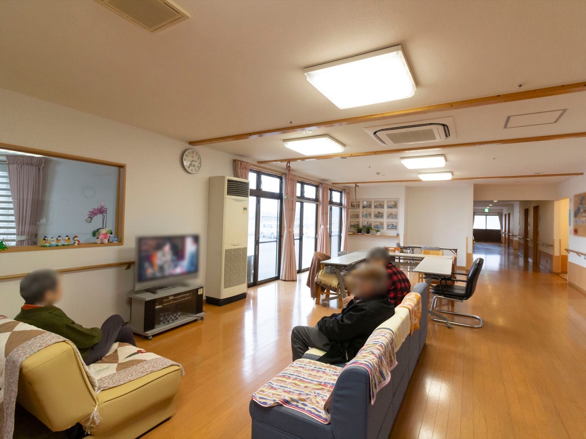 通路脇に広がる空間が共有スペースである。テーブルや椅子、ソファーやテレビがあり、入居者様がくつろいでいる。