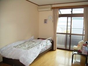 奥のほうに介護用ベッド、エアコンが置いてある小さなワンルームタイプの部屋