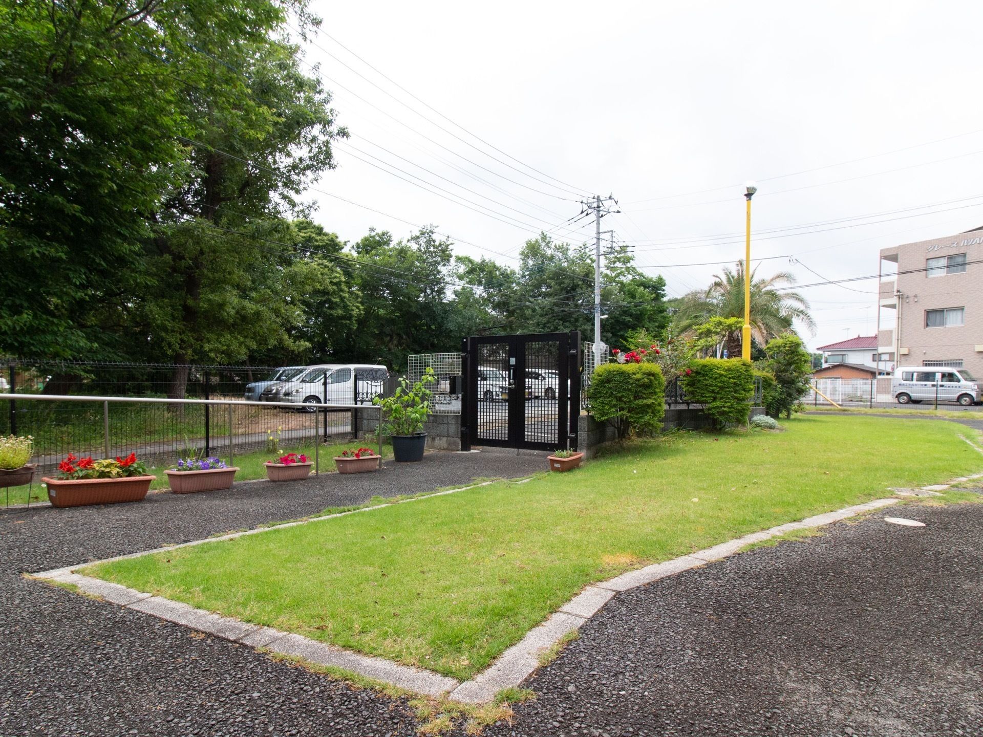 プランターにはさまざまな種類の花が植えられており、駐車場には車が何台も停められている。手すりが備え付けられている。