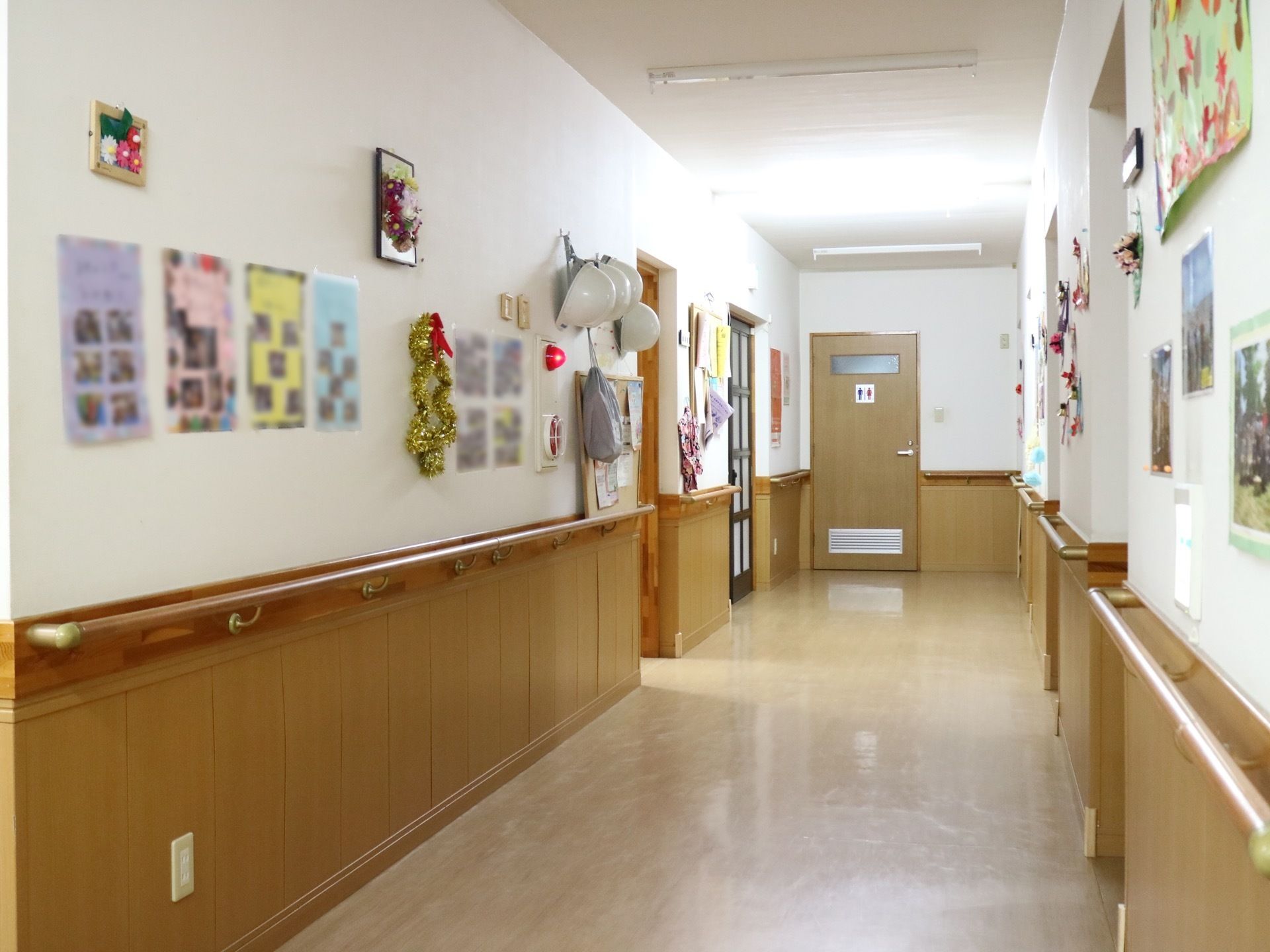 一直線に伸びているビニール床の廊下。壁には手すりが備え付けられており、イベントの写真も飾られている。