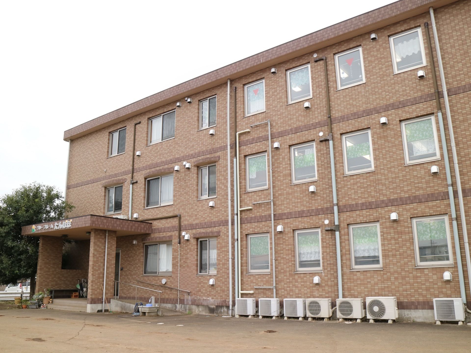 ３階建ての住宅が建っている。茶色を基調としたタイル張りで、玄関の前には手すりの付いたスロープがある。