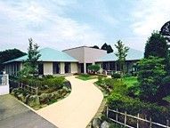 両脇に植栽のあるアプローチと、水色の三角屋根が特徴的な外観の建物