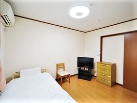 寝具付きのベッドが窓際に置かれ、エアコンやテレビ、タンスなども付いている。