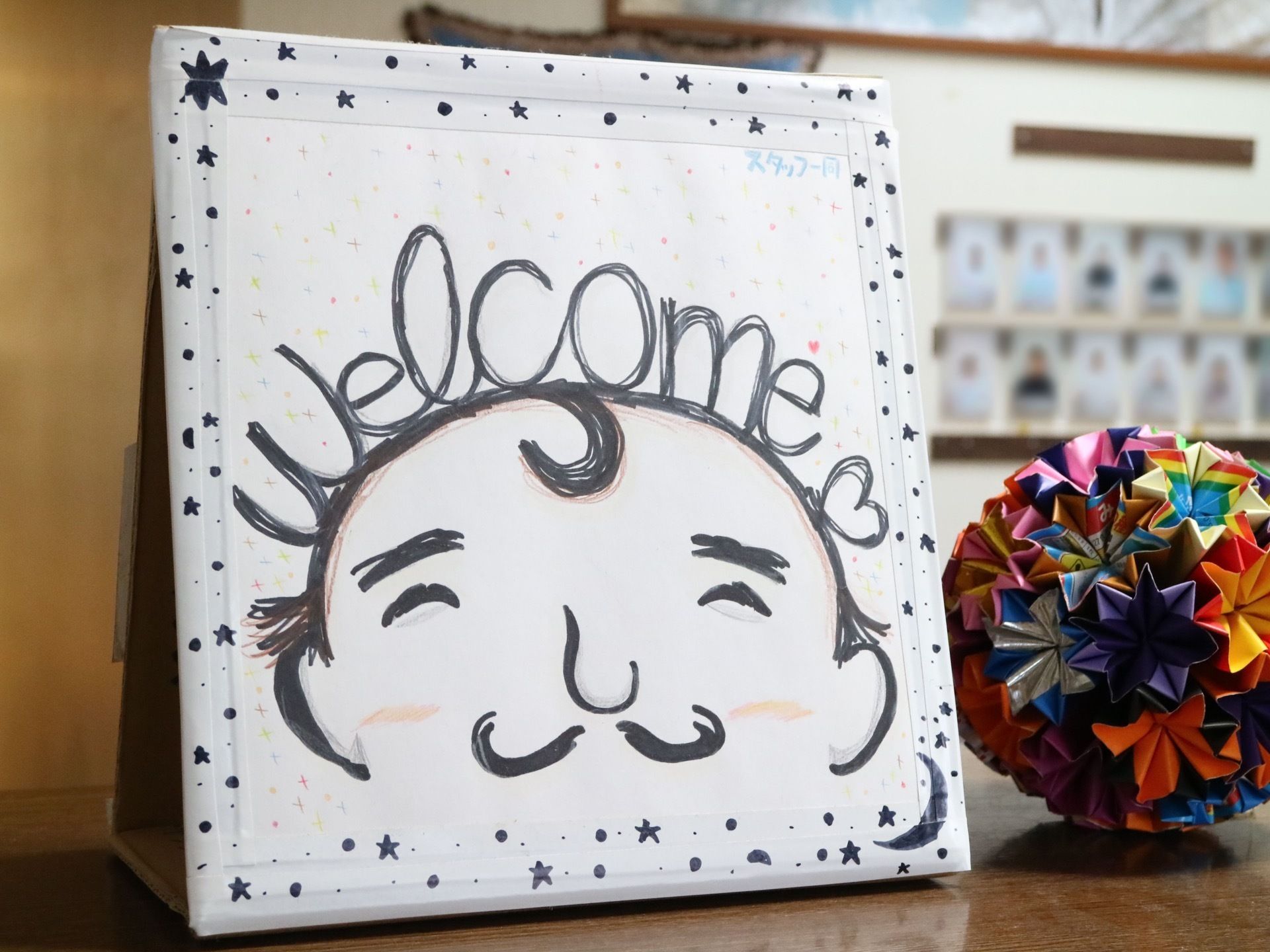 玄関にある受付カウンターには、手書きのウエルカムボードが置かれている。隣には、折り紙で作ったボールも飾られている。