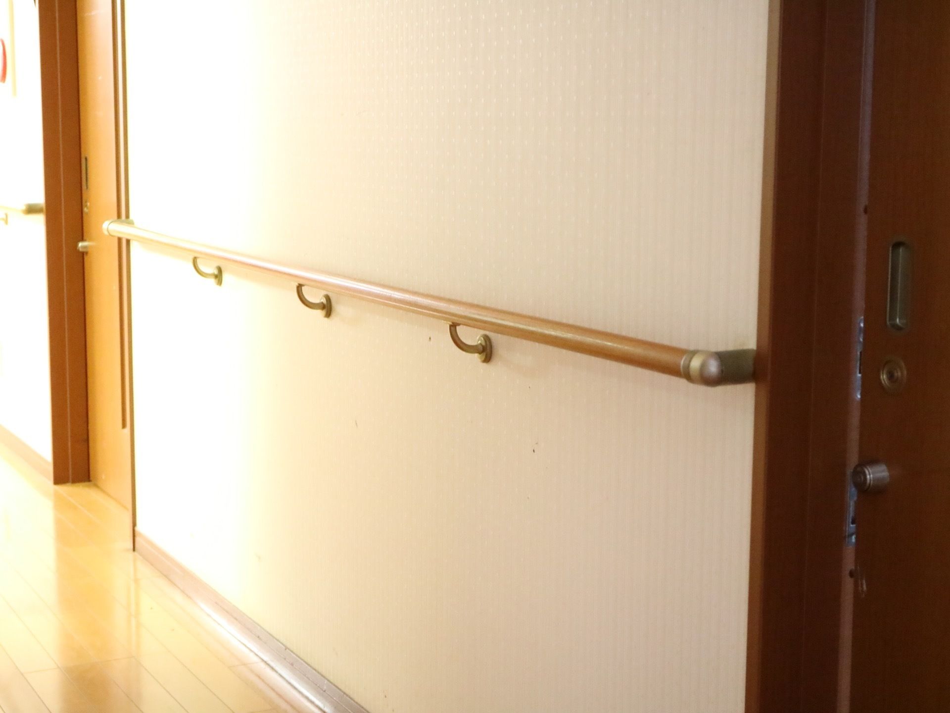 白の壁紙が貼られている通路。居室のドアはスライド式となっており、ドアの横の壁には、木目調の手すりが設置されている。