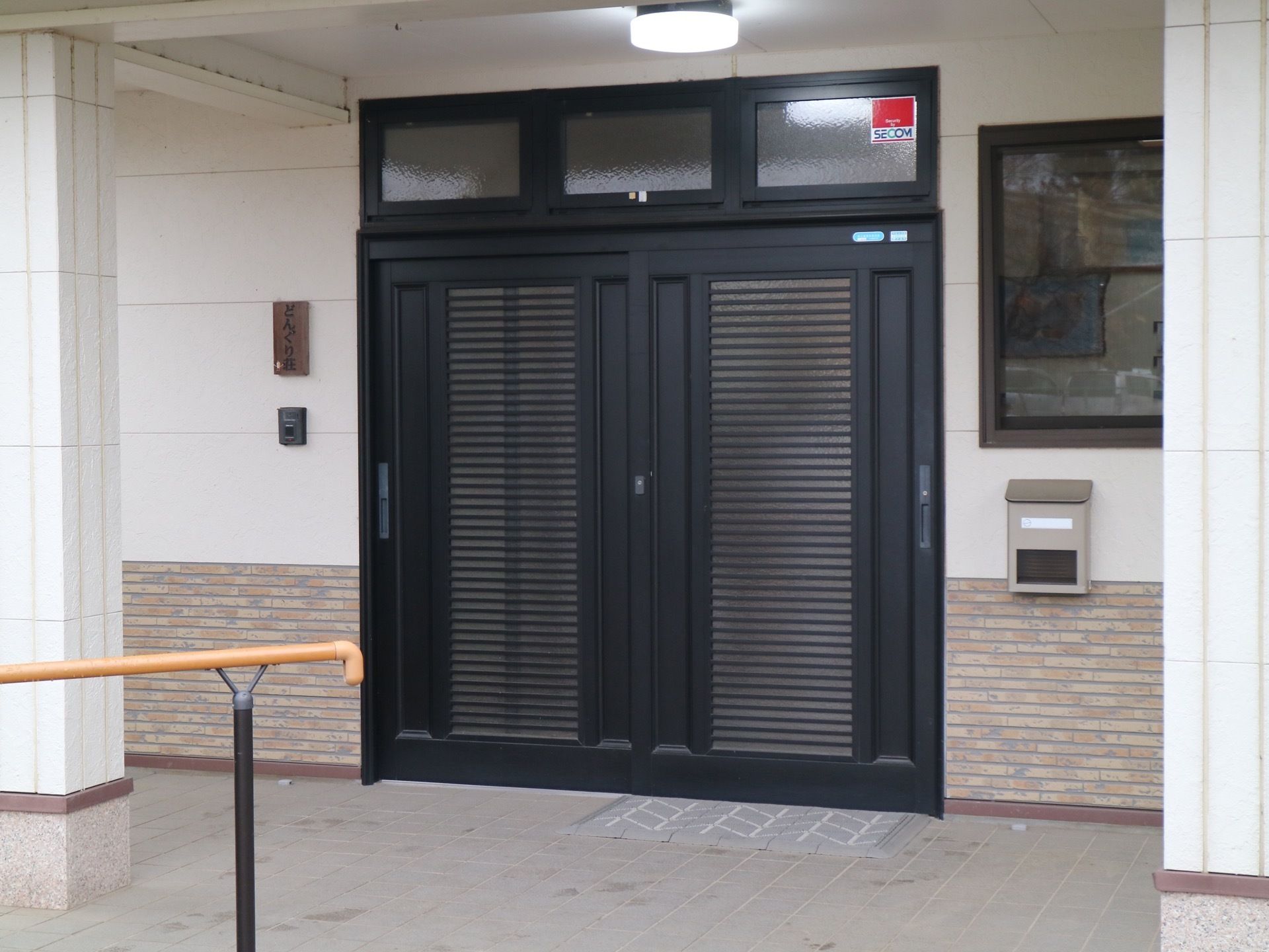 玄関のドアは黒く、スライド式である。ドアの横にはインターフォンが設置され、その上に施設名が書かれた木札がかけられている。