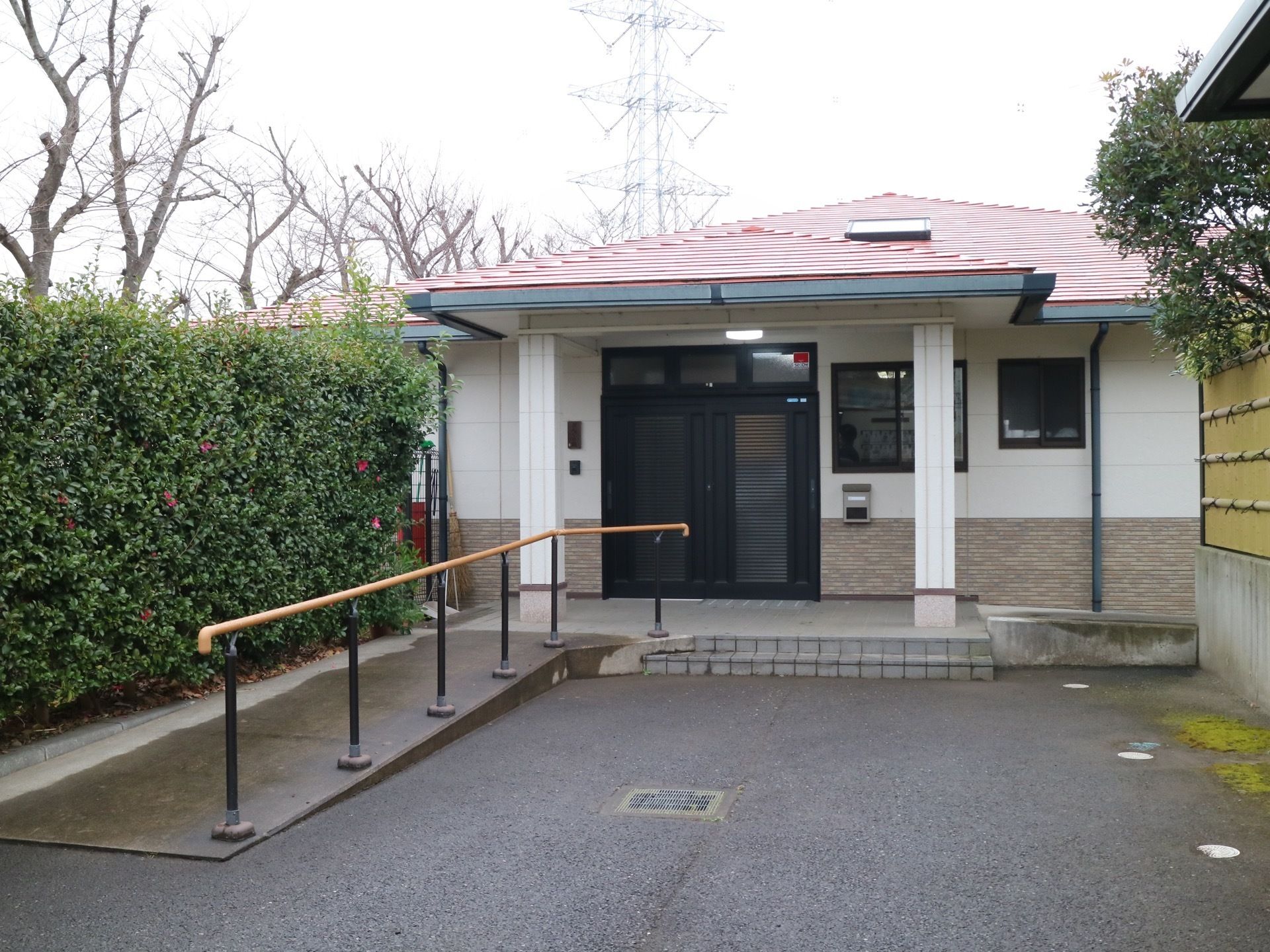 赤い屋根の、平屋建て施設。周囲が樹々などの自然に囲まれている。玄関前には、スロープと階段が設置されている。