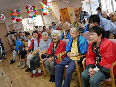 共有スペースにはずらりと椅子が並べられ、赤や青のハッピを着た高齢者たちが座っている。館内にはお祭りの飾りつけがされている。