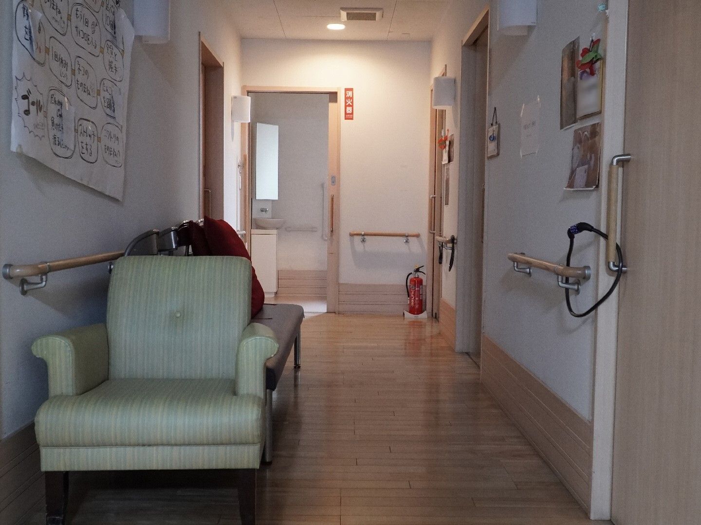 両側の白い壁に手すりがついた途中に椅子が置いてある廊下