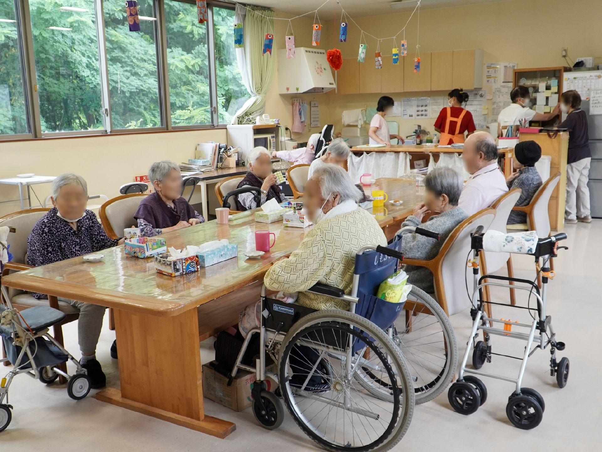 壁一面に大きな窓がある部屋の中央に置かれた長机に座る入居者様
