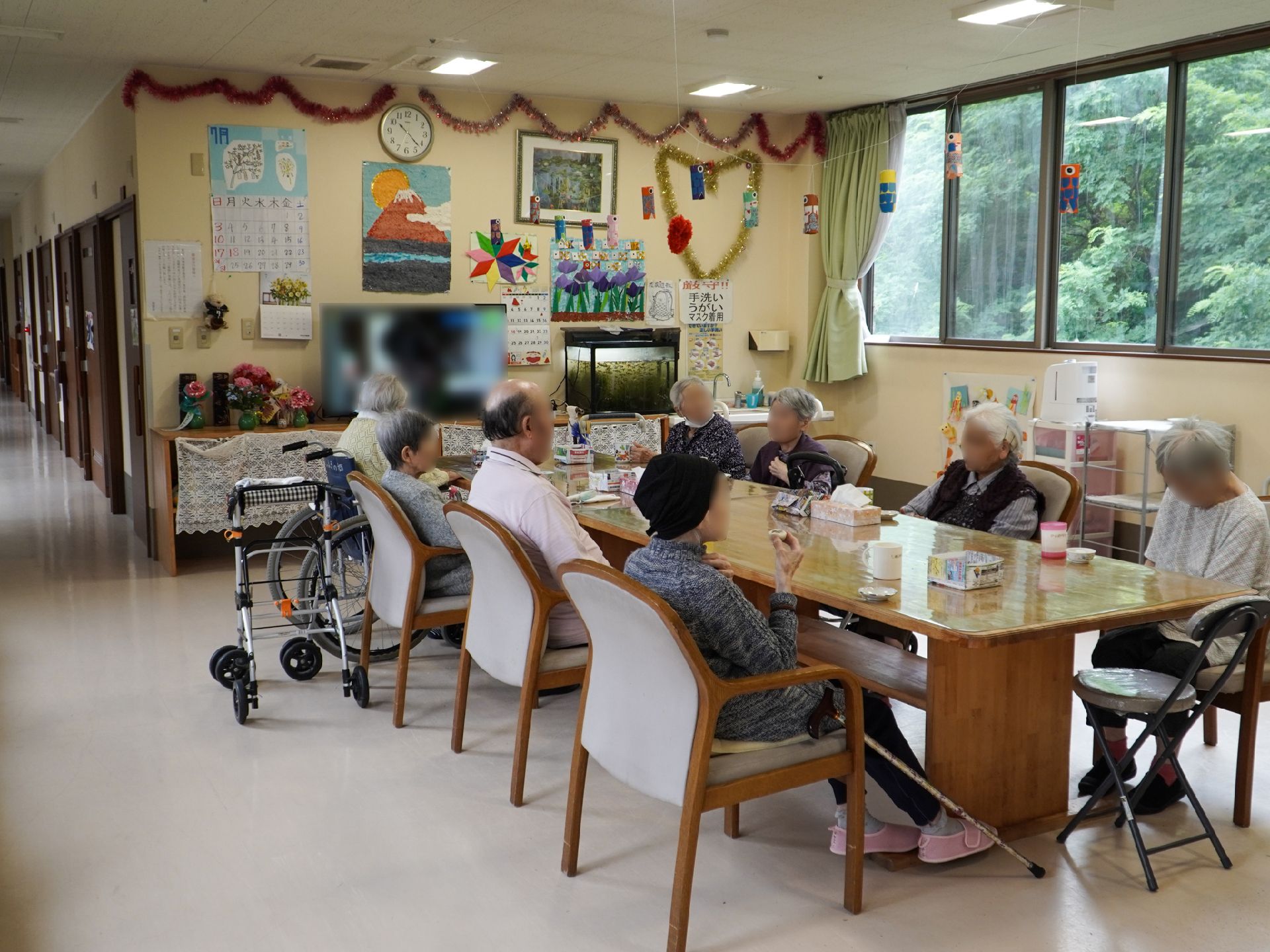 扉のない広間のテレビの前に置かれた長テーブルに座る入居者様