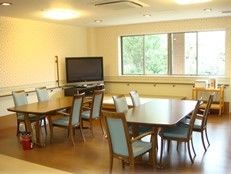 窓がある広めのリビングスペースにテレビ、椅子、テーブルなどが並んでいる様子