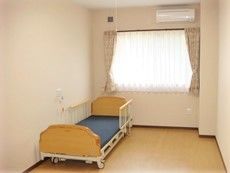 個室にベッドやエアコンがある様子。ベッドのそばに緊急コールが付いているのが分かる