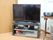 部屋の角に、大型のテレビが置かれており、テレビ台の下の段にDVDプレーヤーがある。横の台の上には、CDラジカセが載っている。