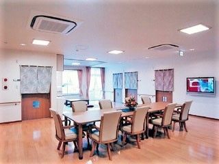 フローリング仕様のリビングルームの様子。長いテーブルと椅子がたくさん並んでいる食堂の様子