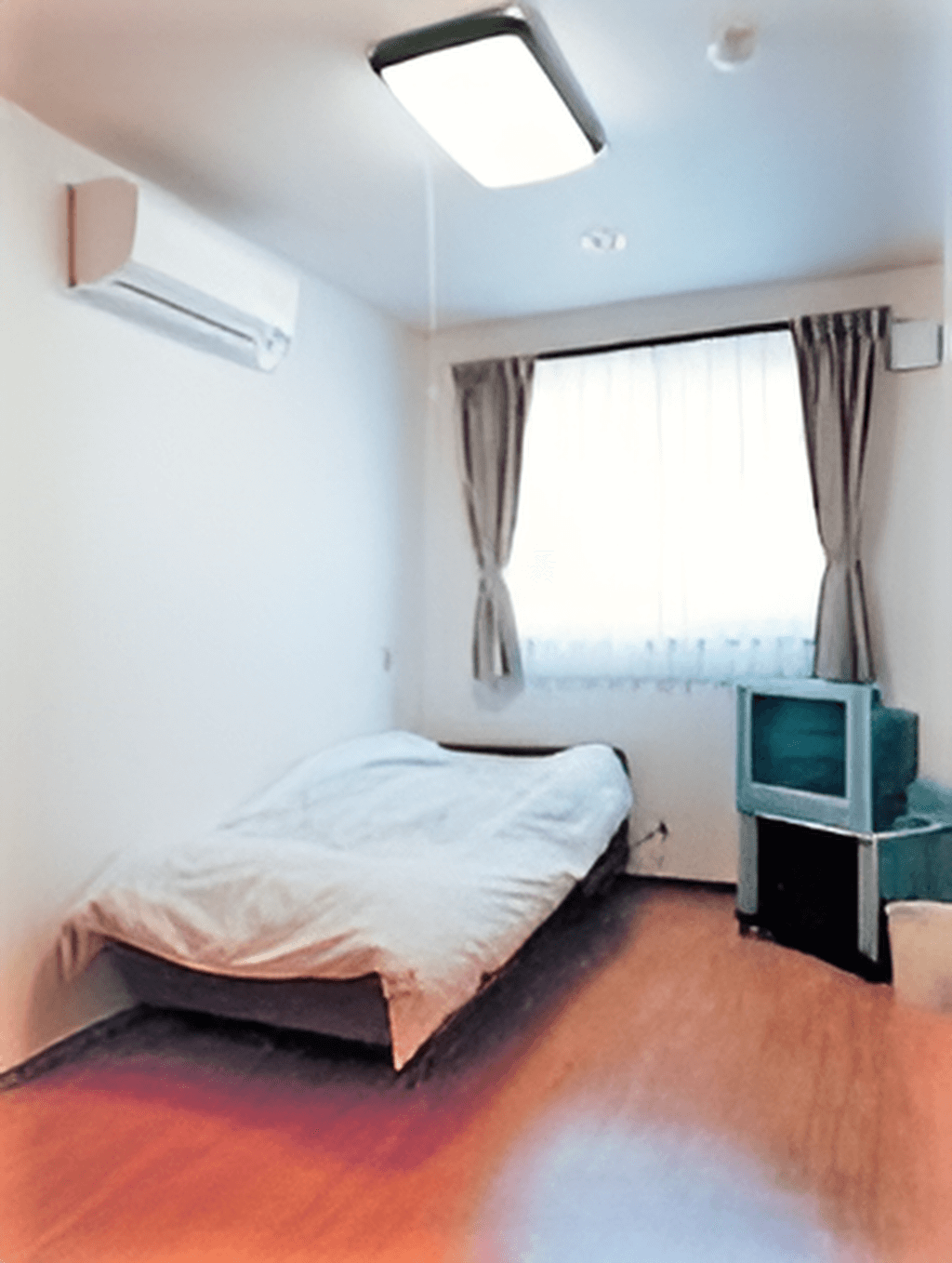 ワンルームの部屋にベッドやテレビ、エアコン、照明がある様子が写っている