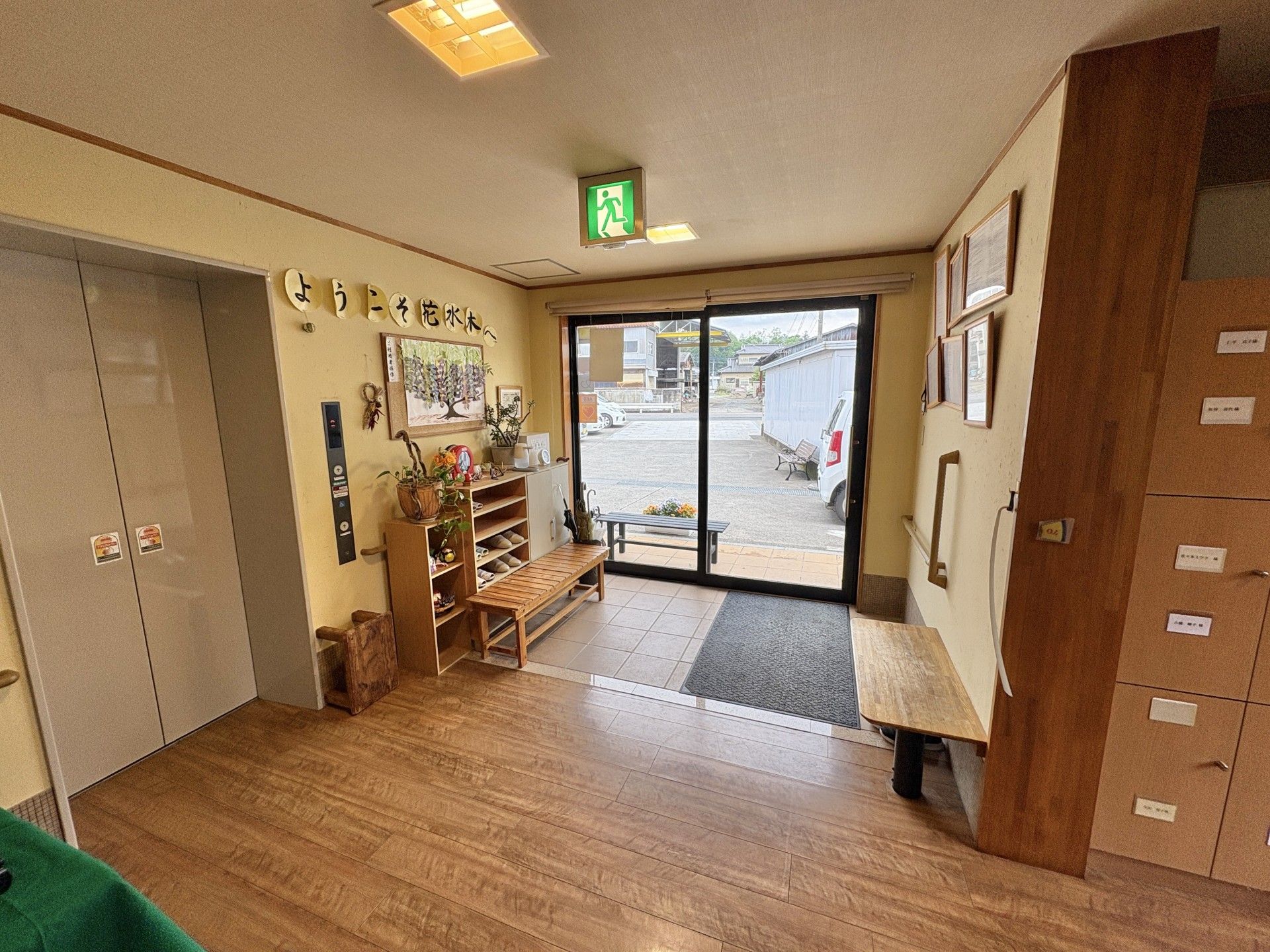 緑の多い屋外で笑顔で過ごしている車いすの高齢女性と付き添いの女性スタッフ。スタッフはブルーのポロシャツを着て女性の手に自分の手を重ねている。
