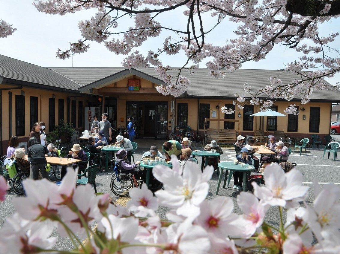 施設敷地内に咲く花ごしに見える利用者の様子。花見をしている利用者
