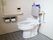 洋式便座が備え付けられた、トイレである。グレーのタイル床が貼られている。背もたれクッション、手すりもある。