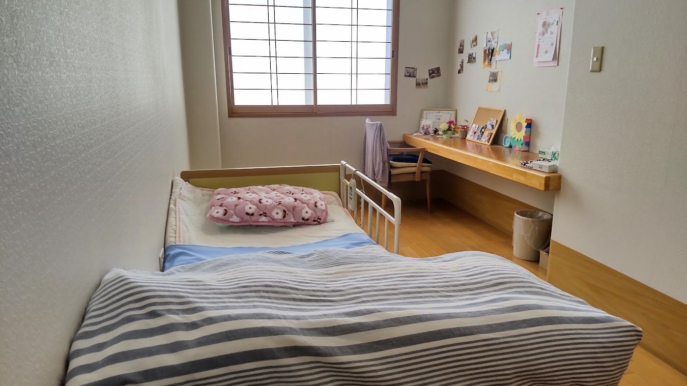 チェックの布団が敷かれたベッドの横にはテーブルやテレビがあり、障子が付けられた大きな窓から日差しが降り注いでいる。