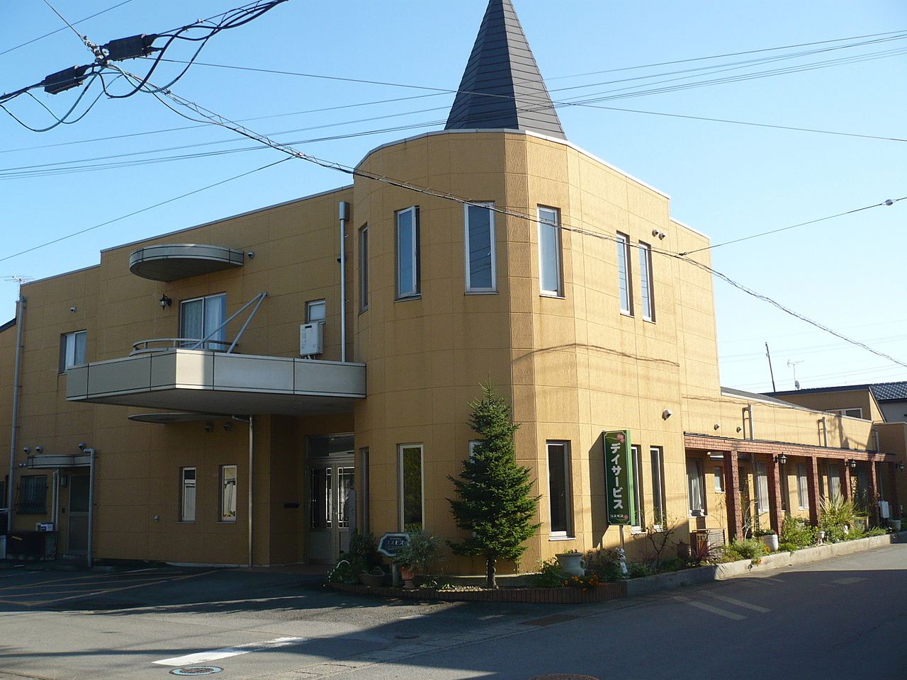 オレンジ系の外壁の建物は一部2階建て、一部平屋建てで、敷地内には駐車場があり、玄関には屋根もある。