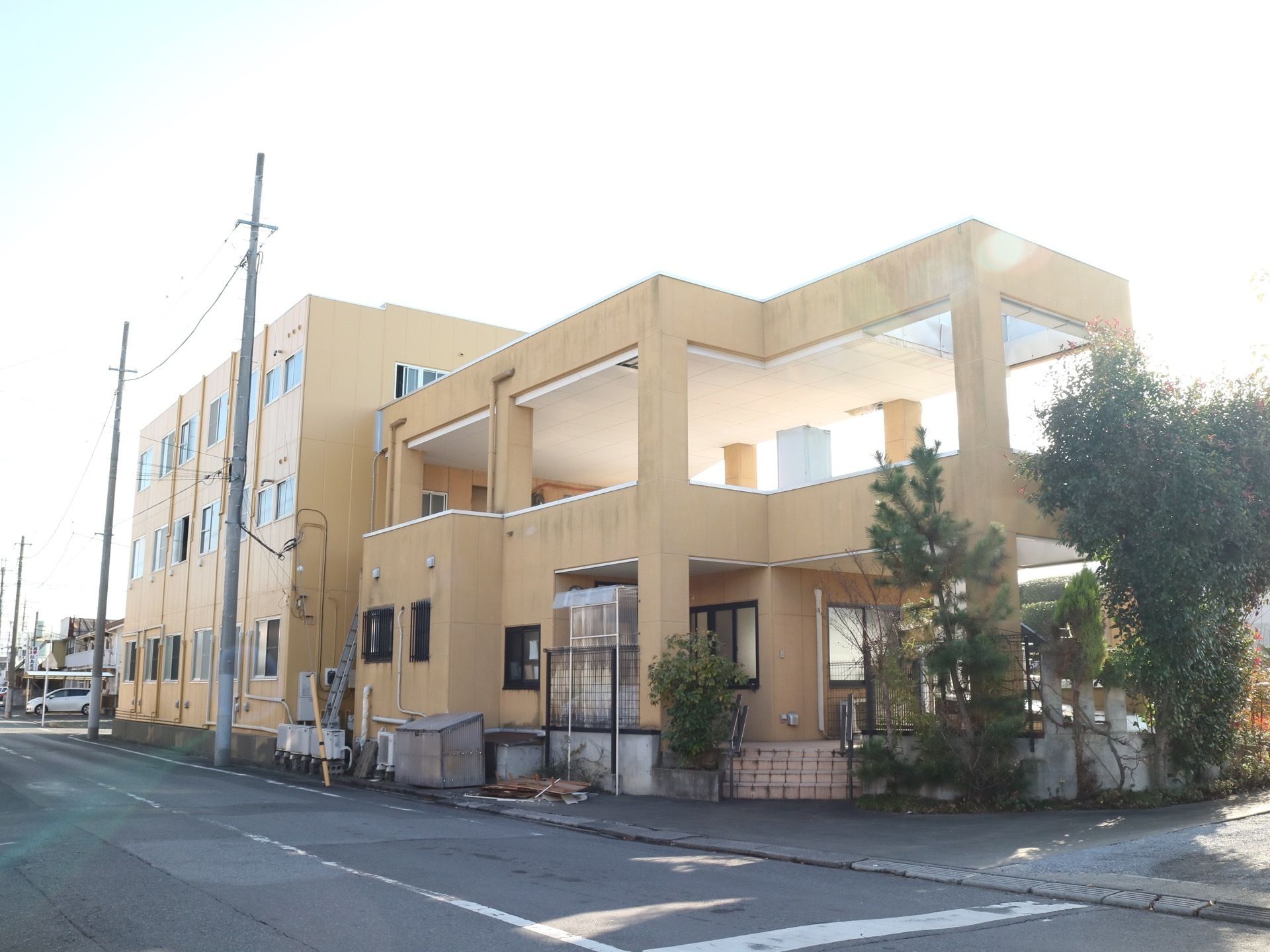 交差点の角に建つ黄色の建物である。食堂部分は平屋で居住部分は３階建てである。玄関前には植込みが整備されている。