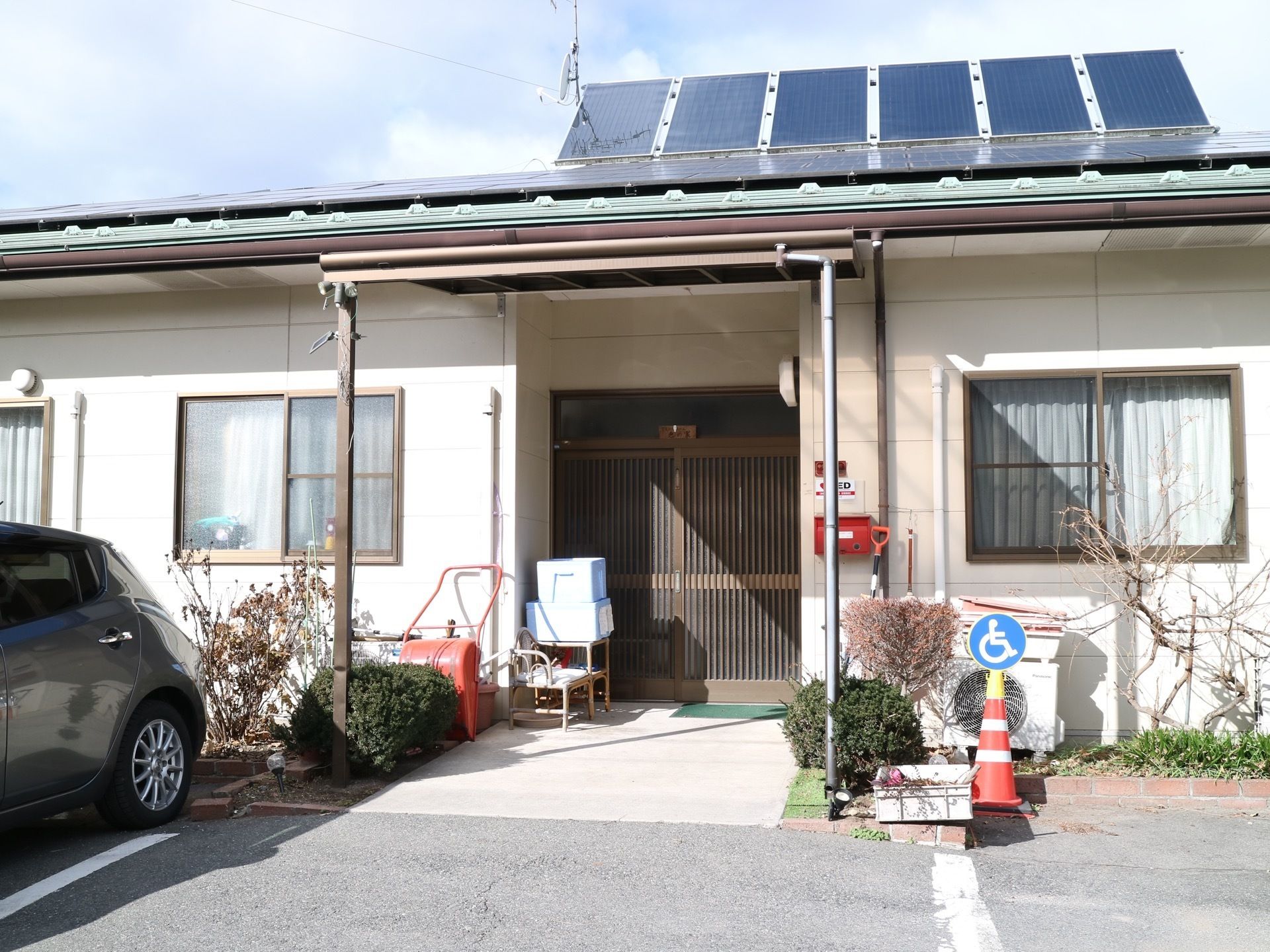 白を基調とし平屋建ての建物で、屋根にはソーラーパネルが設置されている。駐車場には、複数台の車が停められている。