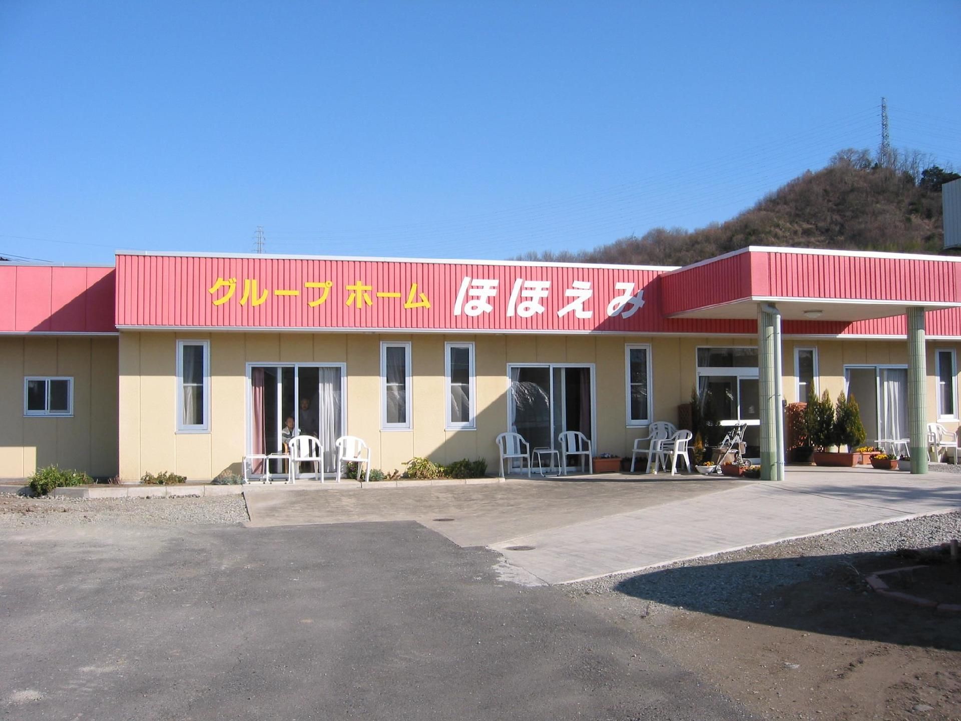広い敷地にピンクの屋根の平屋建ての建物がある。建物周辺には椅子やベンチ、プランターが置かれている。