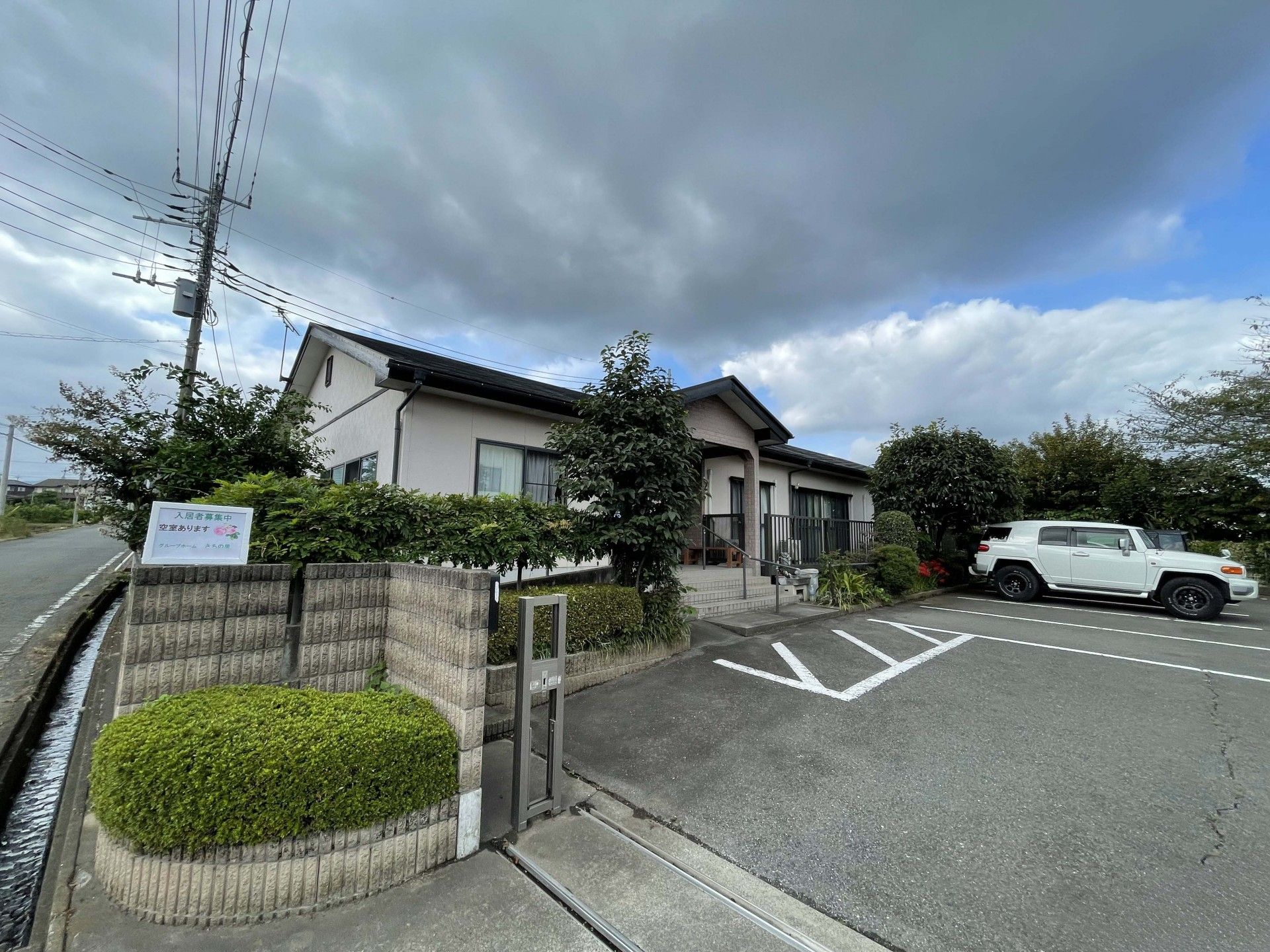 車椅子に乗って手を振る高齢女性と後ろで介助をする男性ヘルパー