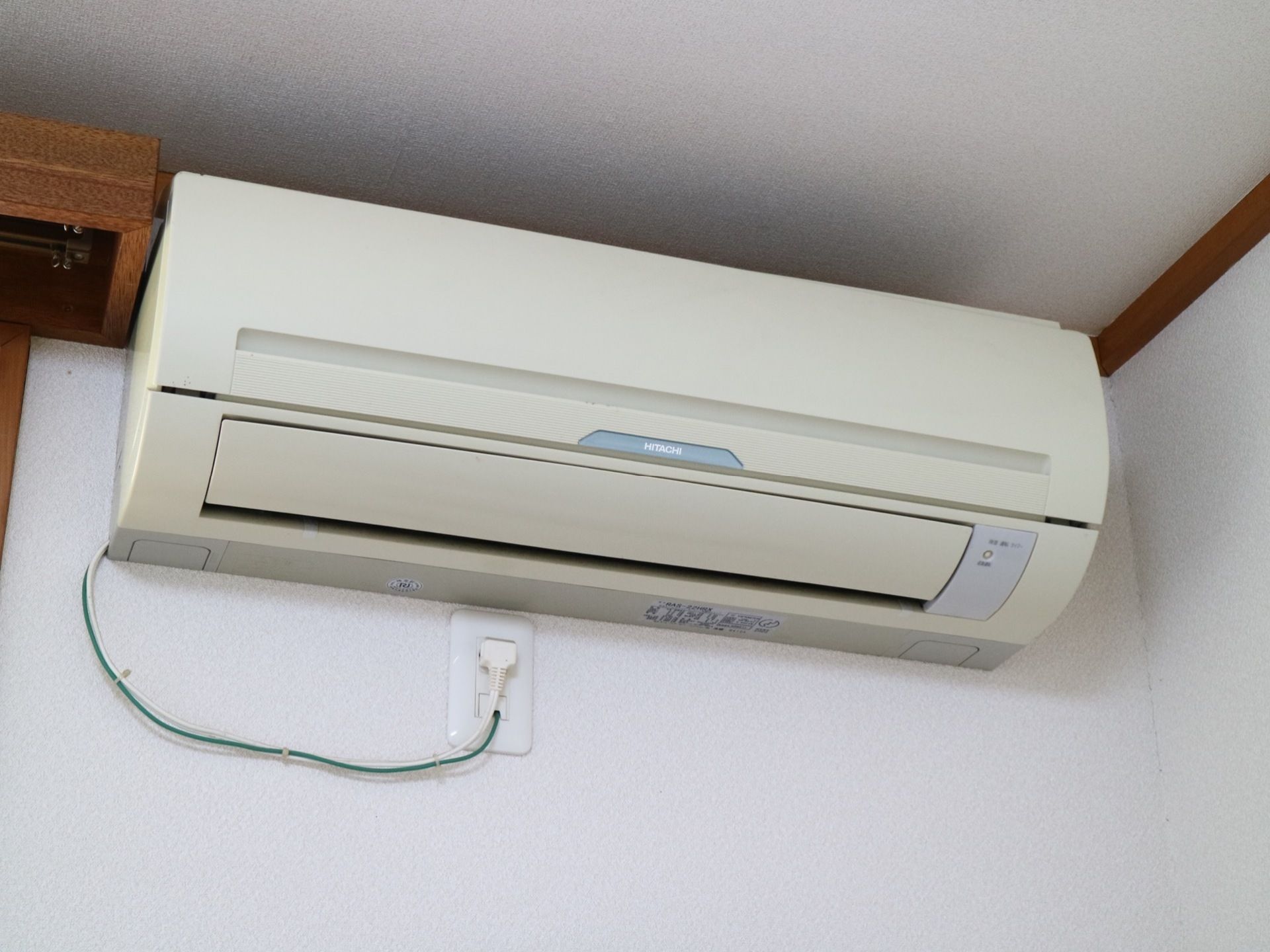 居室などに設置されたエアコンの図である。部屋の角の天井近くに薄いベージュ色のエアコンがかかっている。