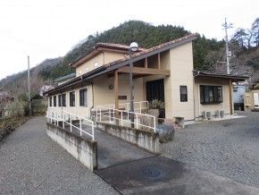 平屋建ての建物で玄関には屋根が付き、玄関には手すり付きのスロープが付いている。