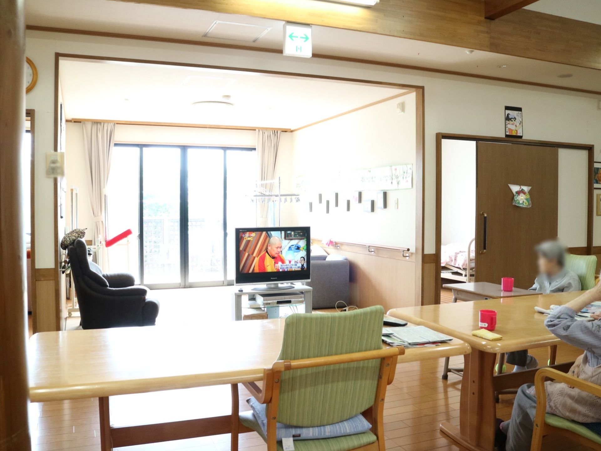 中央奥にある大きな窓からたくさんの外光が差し込む共有スペース。テーブルセットが並び、入居者様がくつろいでいる。