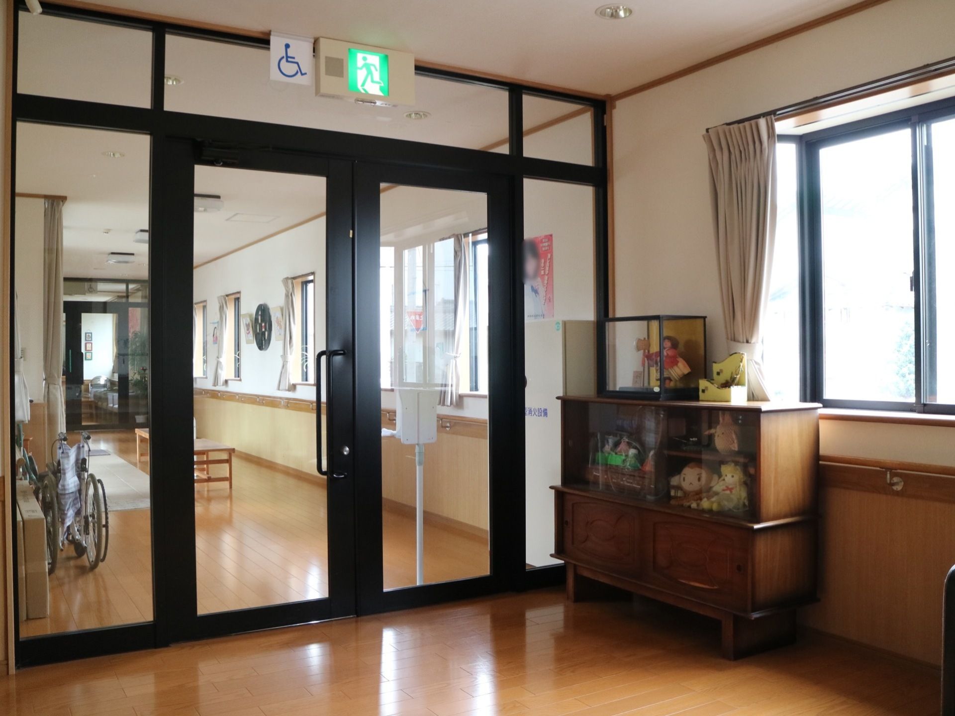 左手奥に黒い枠のガラス扉があり、奥へ向かって廊下が伸びている。入り口前には棚があり、人形などが飾られている。