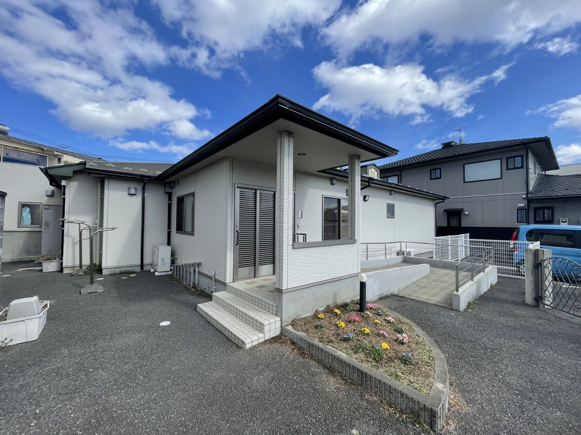 日当たりのいい場所に建っている平屋建ての建物の前に駐車場があり、白い車が止まっている。