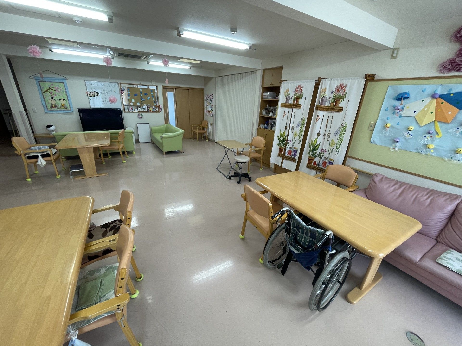 テーブルを囲んで折り紙を折っている高齢の男女。共有スペースの壁には手すりが付いている。