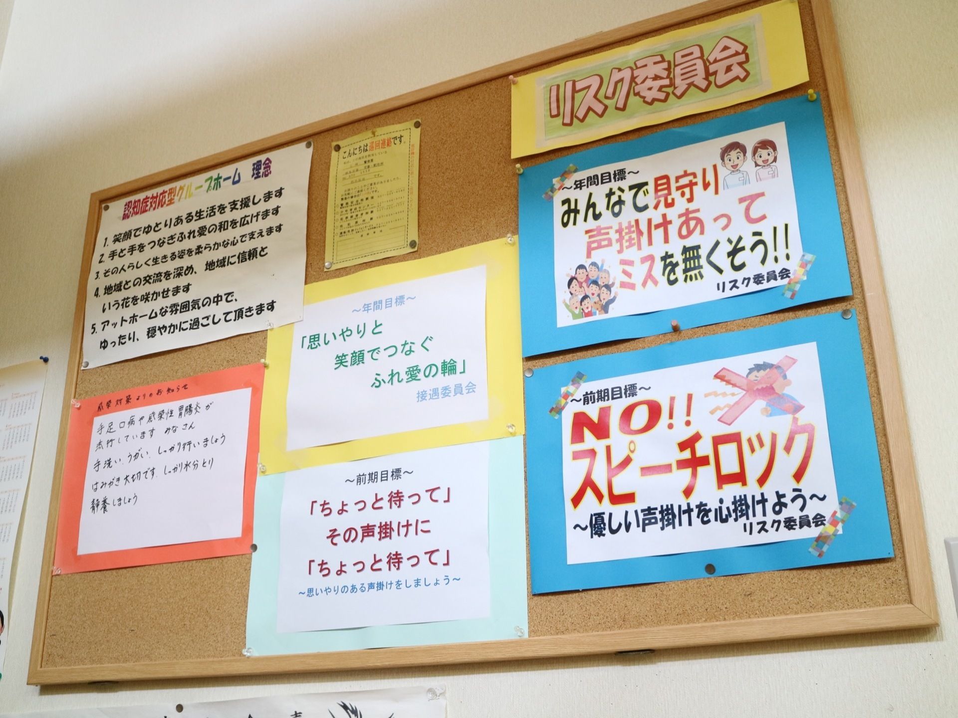 白い壁にコルクボードが貼られている。施設からのお知らせや、標語などが色画用紙と白い紙に貼りだされている。