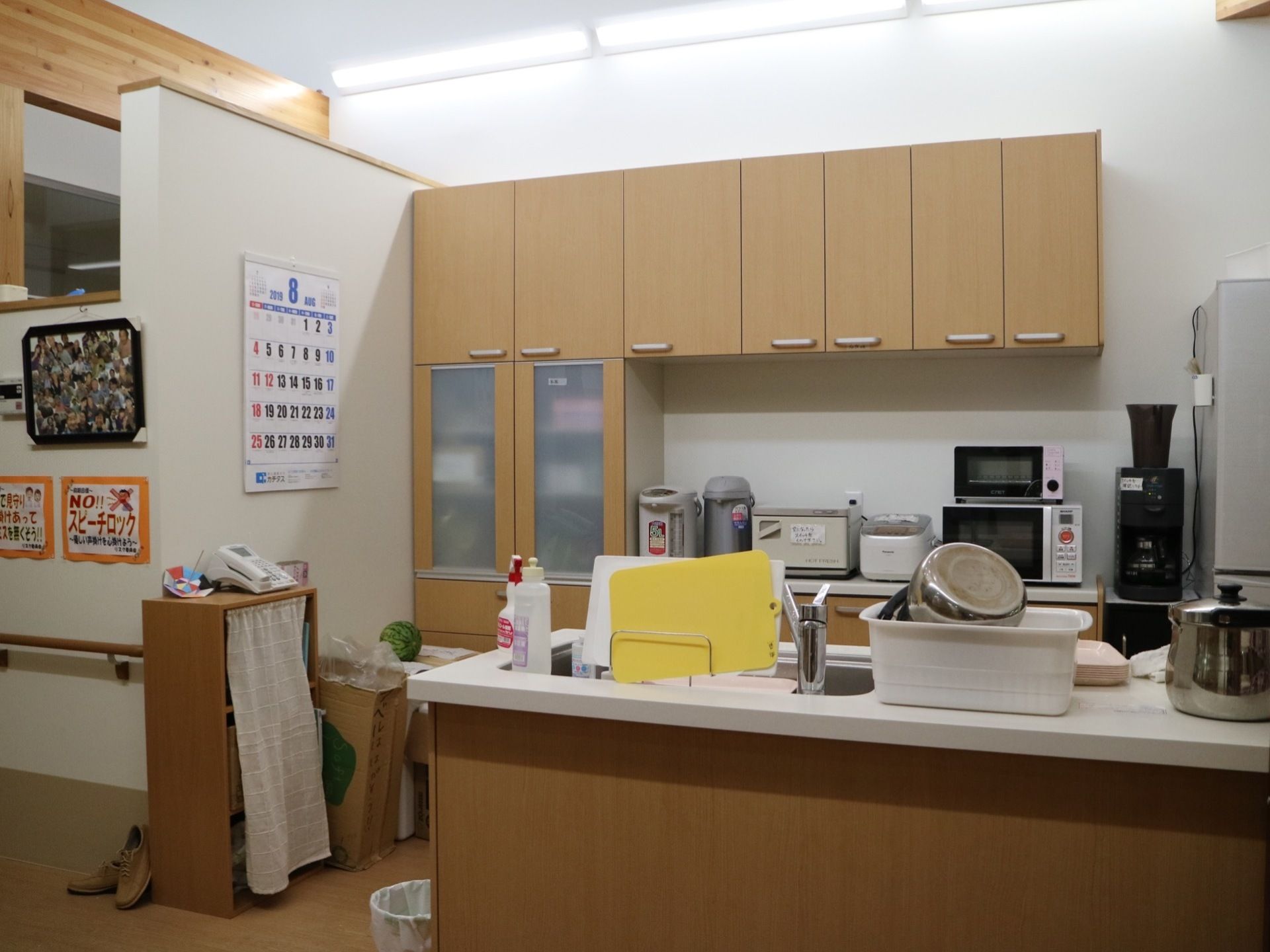 オープンカウンターのキッチンである。奥の壁には食器棚があり、その下に電子レンジや炊飯器が置かれている。